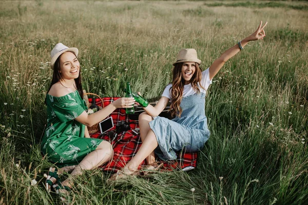 Deux jolies jeunes femmes assises sur la couverture de pique-nique et amusez-vous. Bière et sandwichs . — Photo