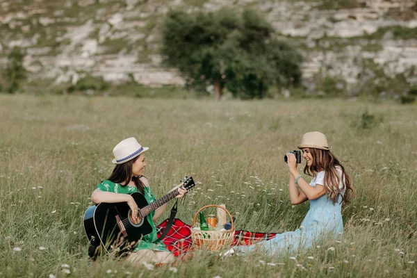 ピクニック毛布の上に座っている 2 つの魅力的な若い女性と楽しい時を過します。音楽と自由の概念. — ストック写真