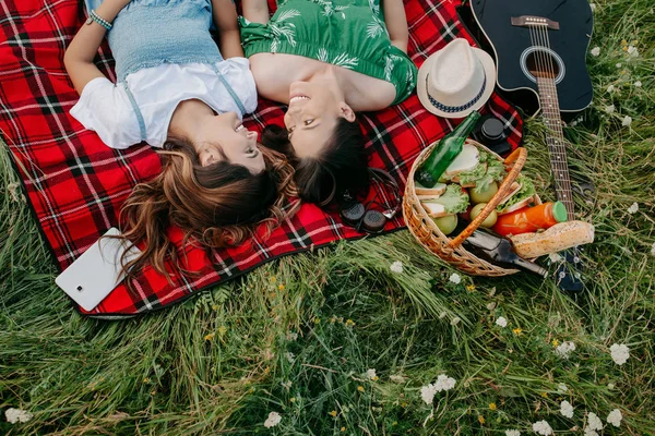 Deux jeunes femmes gaies à la mode allongées sur la couverture de pique-nique et relaxantes . — Photo