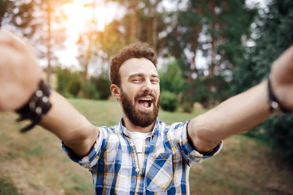 Podekscytowany hipster młody człowiek zrobić selfie w parku na zachód słońca. — Zdjęcie stockowe