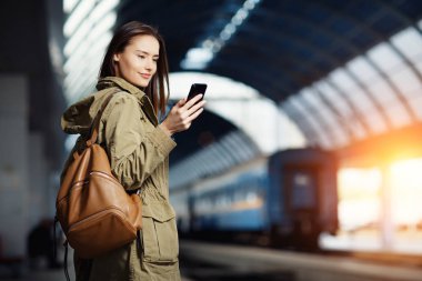 Tren İstasyonu platformu üzerinde duran akıllı telefon kullanan güzel genç kadın.