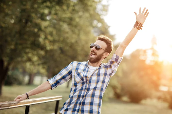 Gelukkig vieren bebaarde man met zonnebril poseren met handen upin het park. — Stockfoto