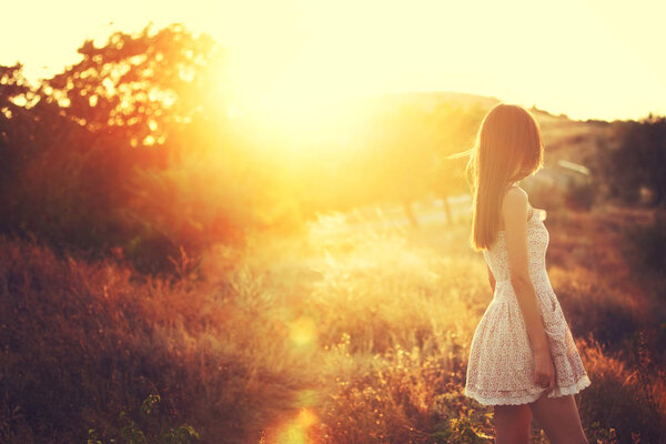 Beautiful young girl in a white dress enjoying the sunset light. Sunrise time