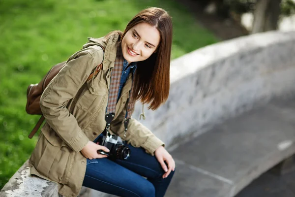 Young beautiful woman sitting on bench in park. Traveler with vintage camera — Stock Photo, Image
