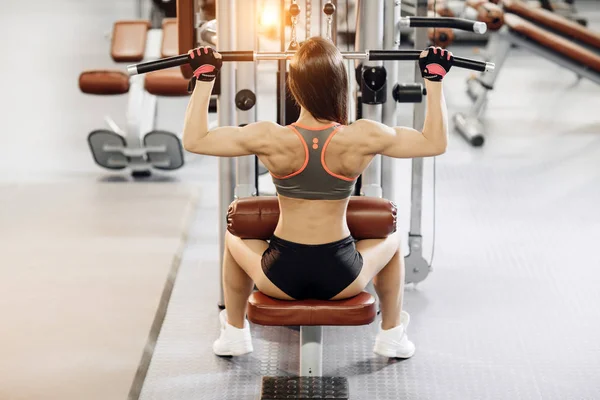 Jovem mulher trabalhando na máquina lat pulldown no ginásio , — Fotografia de Stock