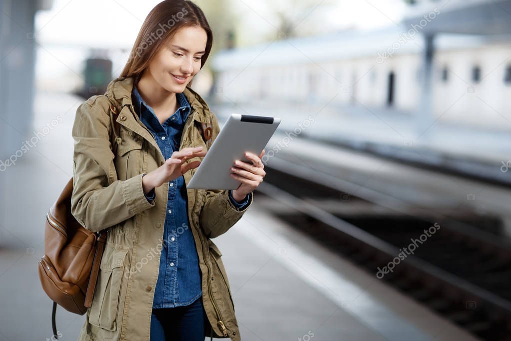 Young woman with backpack using tablet while standing on the railway station platform.