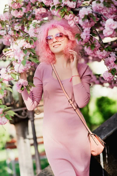 Güzel genç kadın kıvırcık saçları ve güneş gözlüğü yakın ağaç bahar çiçek açması ile.