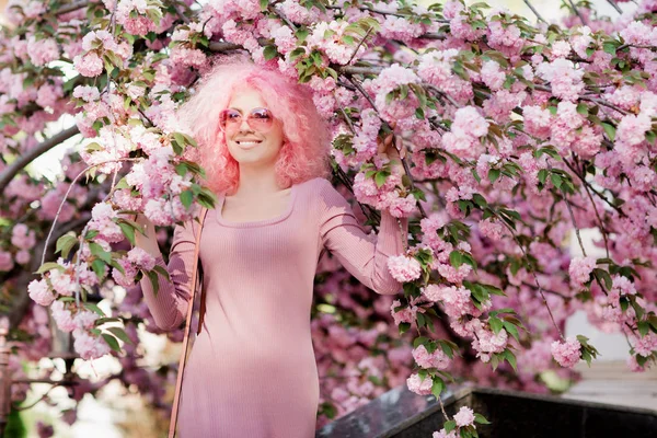 Güzel genç kadın kıvırcık saçları ve güneş gözlüğü yakın ağaç bahar çiçek açması ile.