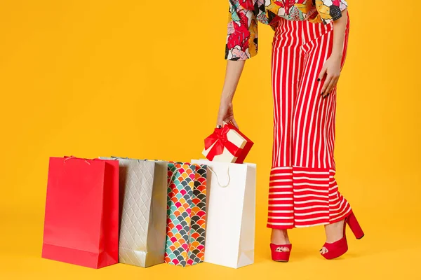 赤パンツとサンダル オレンジ色の背景上のカラフルなショッピング バッグ、ギフト ボックスを保持している女性の画像をトリミング. — ストック写真