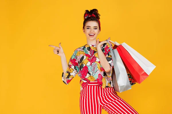 Молодая счастливая белая женщина в повседневной красочной одежде держит сумки и покупки на оранжевом фоне . — стоковое фото