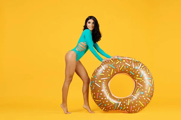 Retrato de lenhts completos de una mujer fitness brillante vestida con traje de baño posando con anillo inflable sobre el fondo naranja . — Foto de Stock