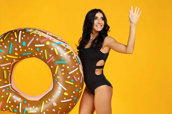 Heyecanlı bir genç kadın görüntüsünü Siyah mayo turuncu zemin üzerine şişme halka ile poz giyinmiş.