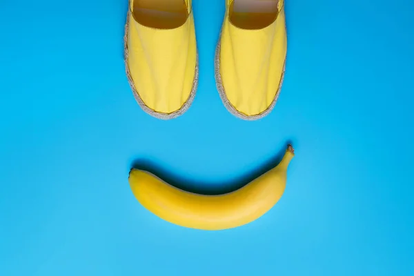 Gelbe Sommerschuhe und Banane auf blauem Hintergrund. Lächeln-Emoji-Konzept. — Stockfoto