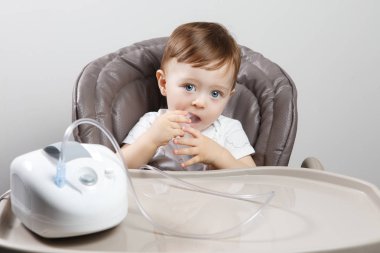 Kullanarak bir yüksek sandalyede oturan sevimli küçük oğlu Nebulizatör. Sağlık kavramı.