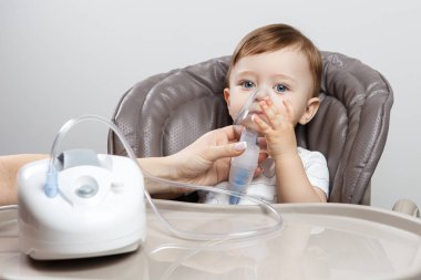 Anne, sandalyede oturan küçük sevimli çocuk için nebulizör kullanıyor. Sağlık hizmeti kavramı