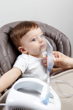 Anne, sandalyede oturan sevimli bebek için nebulizör kullanıyor. Sağlık hizmeti kavramı.