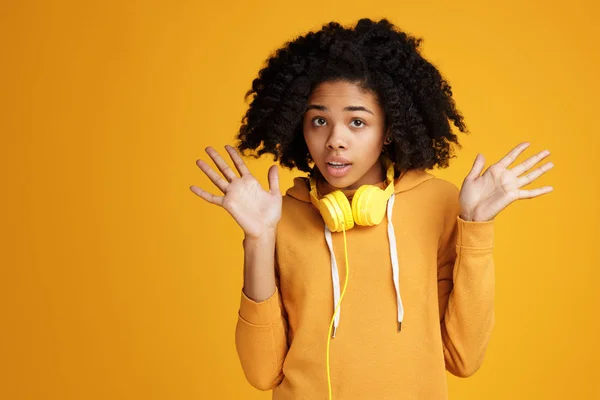Schockierte junge Afroamerikanerin in lässiger Kleidung und Kopfhörer vor gelbem Hintergrund. — Stockfoto