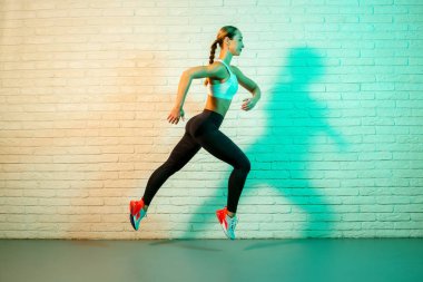 Sportif, genç ve çekici bir kadın. Neon ışıklarıyla ön tuğla duvarda koşuyor..