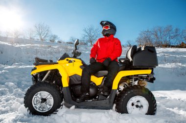 Sürücü kırmızı sıcak kış giysili genç adam ve siyah kask Atv 4wd quad bisiklet üzerinde stand ile derin tekerlek iz şiddetli kar yağışı. Moto kış sporları.