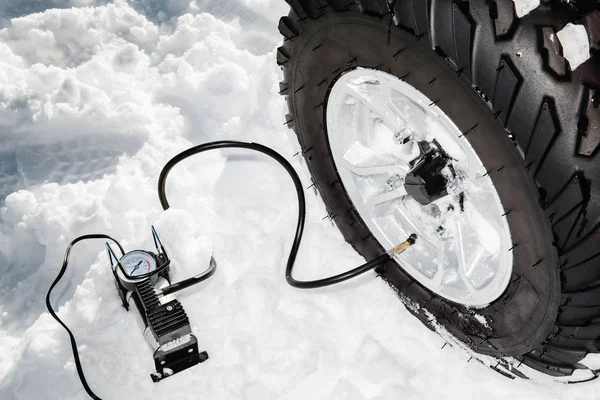 Проверяю давление в шинах. Перекачка воздуха в автоматическое колесо на квадроцикле ATV 4wd стоять в сильном снегу. — стоковое фото