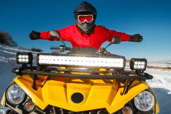 Photo of attractive young man in red warm winter clothes and black helmet with arms open on the ATV 4wd quad bike stand in heavy snow with deep wheel track. Moto winter sports. — Stock Photo, Image