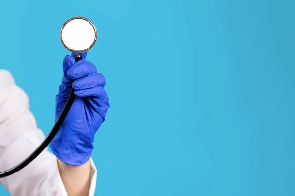 Close-up foto van jonge vrouw arts hand in handschoenen met behulp van de stethoscoop op blauwe achtergrond. — Stockfoto