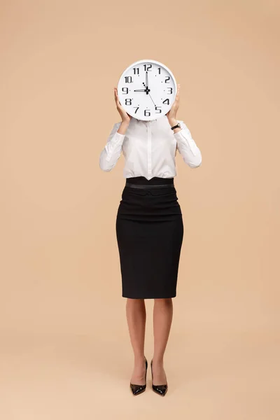 Photo of young modern business woman hold a clock in front of the face over beige background. — Stock Photo, Image