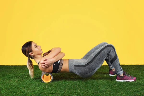 Photo amazing fit young woman do exercise with foam roller on green grass over yellow background. — Stock Photo, Image