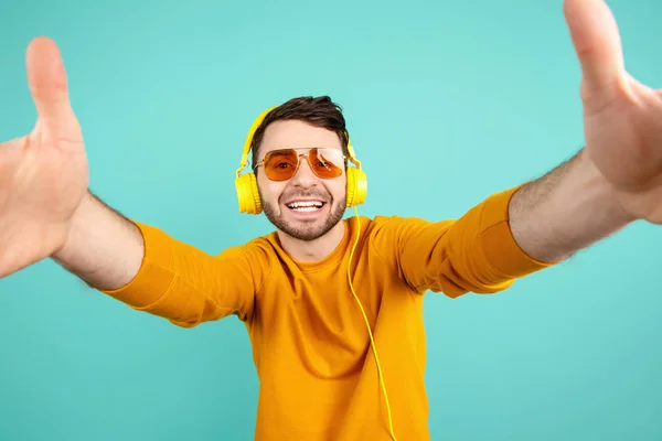 Gelukkige baard jonge man draagt gele zonnebrillen luisteren naar muziek met gele koptelefoon en neem sefie over cyaan achtergrond. — Stockfoto