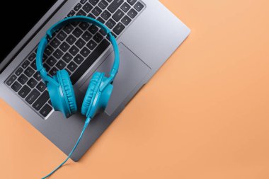 Modern bilgisayar veya dizüstü bilgisayar ve bej arkaplan üzerine mavi kulaklık..