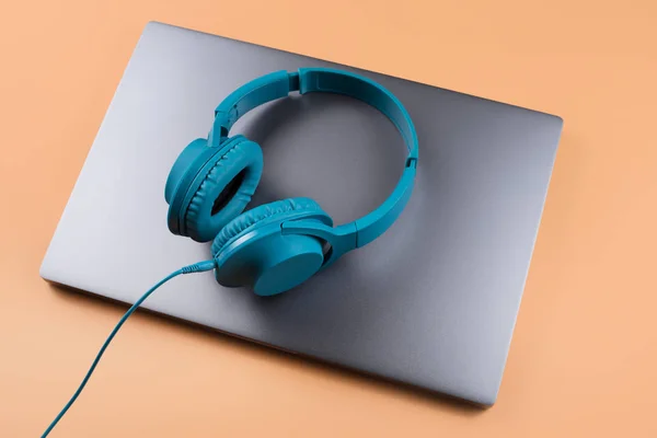 Fotografie stylového moderního počítače nebo notebooku a modrých azurových sluchátek na béžovém pozadí. — Stock fotografie