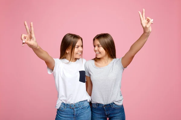 Jolies deux jeunes sœurs jumelles avec un beau sourire avec les mains en l'air montrant un geste de paix sur fond rose . — Photo