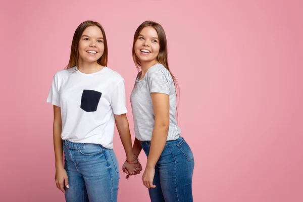 Parlak iki genç ikiz kız kardeş ile güzel gülümseme yürüyüş üzerinde pembe arka plan. — Stok fotoğraf