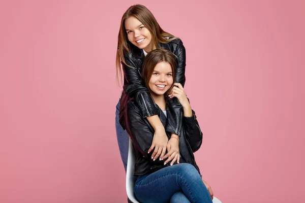 Pembe arka planda güzel gülümseme sarılmak ich ile deri ceketler büyüleyici iki genç ikiz kız görüntü. — Stok fotoğraf