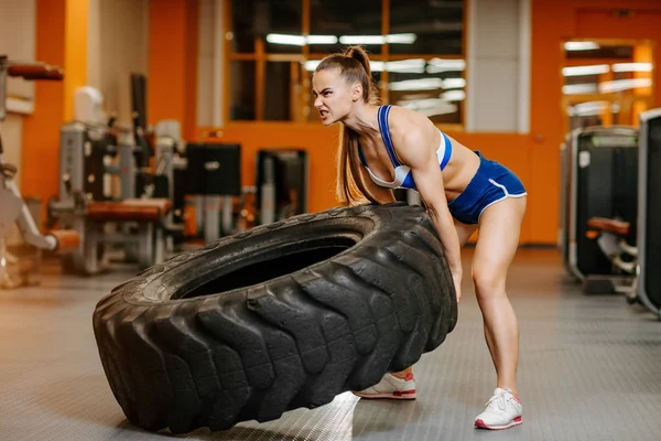 适合年轻女子在健身房锻炼与拖拉机轮。强壮的女人翻动轮胎。健身理念. — 图库照片