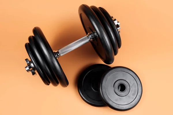 Professional dumbbell and weight plates over beige background. Black metal dumbbell with chrome silver handle. Gym equipment. Fitness concept.