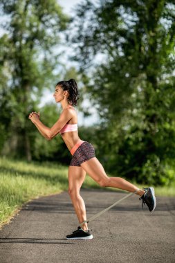 Genç sportif kadın lastik bantla dışarıda egzersiz yapıyor..