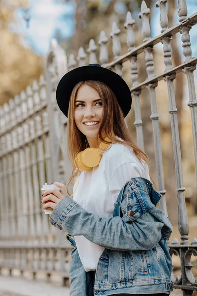 Bir şapka giymiş ve fincan çay ya da kahve parkta tutan kahverengi saçlı güzel bir gülümseyen hippi kız fotoğrafı