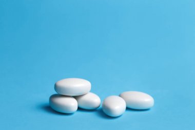 Mavi arka planda bir yığın beyaz hap. Tıp, eczacılık ve sağlık konsepti.