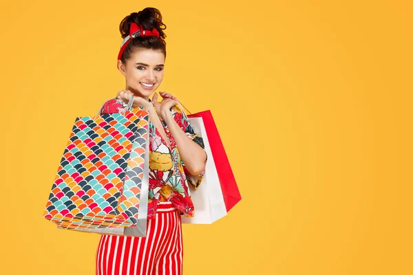 Jovem mulher caucasiana feliz em roupas coloridas casuais segurando sacos e compras sobre fundo laranja. Conceito de compras e vendas . — Fotografia de Stock