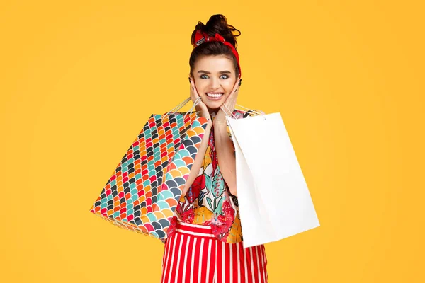 Chockad ung kaukasisk kvinna i casual färgglada kläder som håller påsar och shopping över orange bakgrund. Shopping och säljkoncept. — Stockfoto