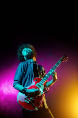 Neon ışıklar kırmızı gitar ile kıvırcık saçlı genç hipster adam. Rock müzisyeni elektrik gitar çalıyor.