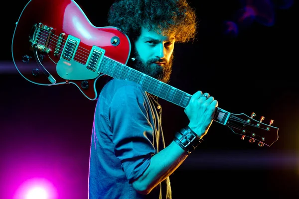 Close-up photo of hipster man with red guitar in neon lights. Rock musician is playing electrical guitar.