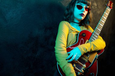 Neon ışıklar kırmızı gitar ile kıvırcık saçlı Moda genç hipster kadın. Rock müzisyeni elektrik gitar çalıyor. 90'ların stil konsepti.