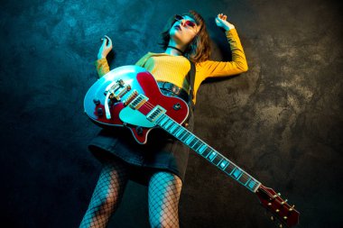 Fashion young hipster woman with curly hair with red guitar in neon lights. Rock musician is playing electrical guitar. 90s style concept. clipart