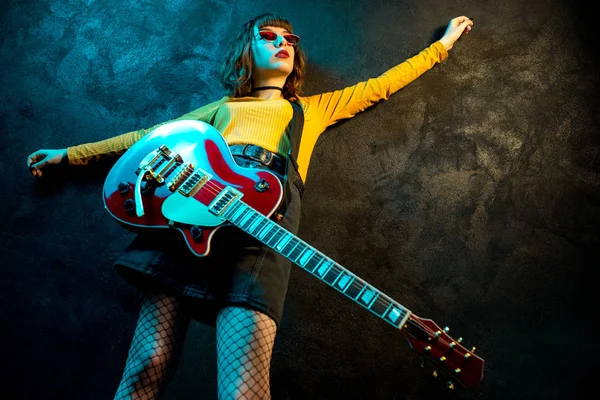 Neon ışıklar kırmızı gitar ile kıvırcık saçlı Charming hipster kadın. Rock müzisyeni elektrik gitar çalıyor. 90'ların stil konsepti.