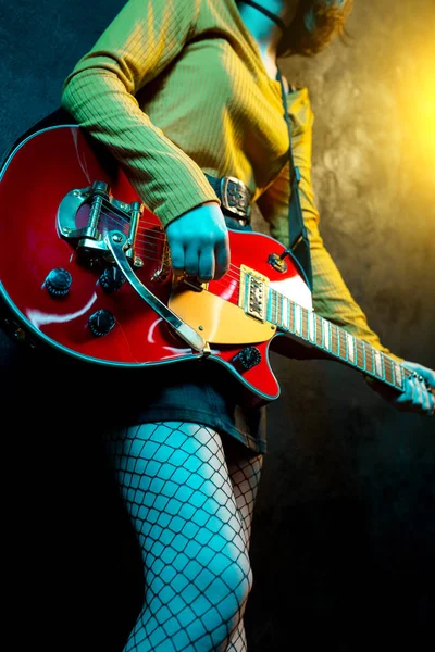 Close-up foto van jonge hipster vrouw benen en rode gitaar in neonlichten. Rock muzikant speelt elektrische gitaar. 90s stijl concept. — Stockfoto