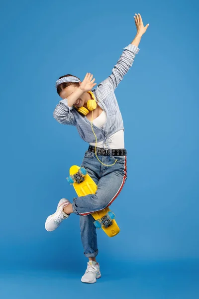 Full längd foto av lycklig bekymmerslös ung kvinna med gult öre eller skateboard och hörlurar badda över Blå bakgrund. — Stockfoto