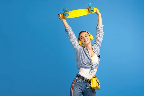 Foto av lycklig ung kvinna hålla gula öre eller skateboard Dans över Blå bakgrund. — Stockfoto