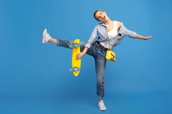 Full längd foto av lycklig ung kvinna med gula öre eller skateboard Dans över Blå bakgrund. — Stockfoto